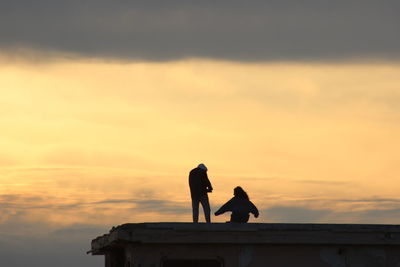 Silhouette couple standing against orange sky