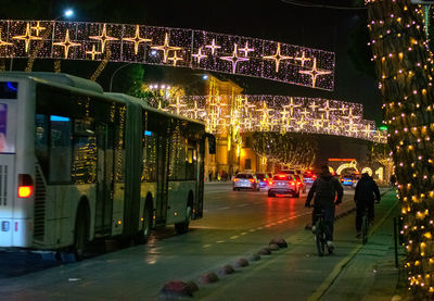 Rear view of people walking on illuminated street at night