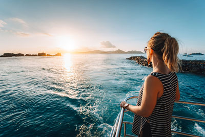 Woman standing by sea against sky during sunset