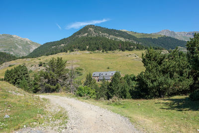 Road amidst trees and mountains against blue sky