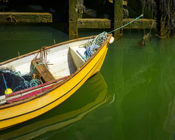 Yellow rowing boat moored up by rope and reflections in the water