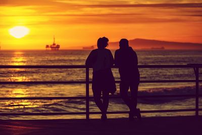 Rear view of silhouette people standing by railing against sea during sunset