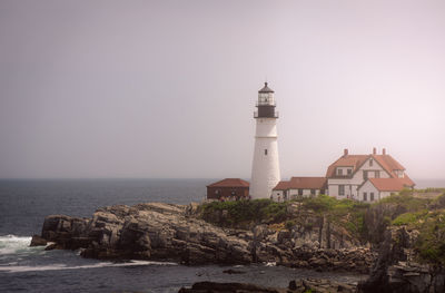 Lighthouse by sea against buildings
