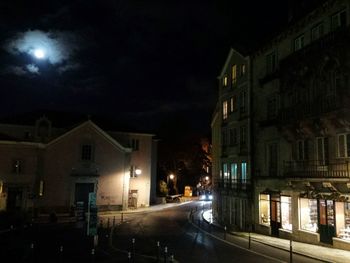 Illuminated street amidst houses against sky at night