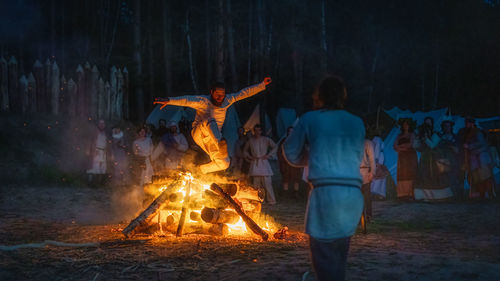 Group of people by bonfire in forest at night