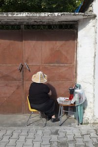 Rear view of man sitting on chair at footpath