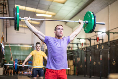 Muscular guy lifting barbell in modern gym