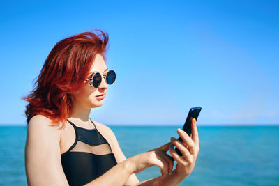 Young woman using mobile phone against sea
