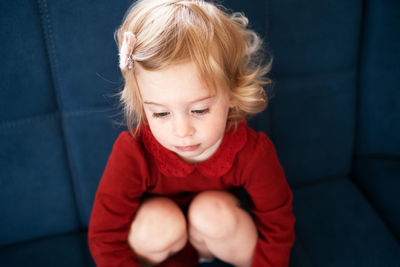 Sad cute baby girl, toddler with blond curly hair hugging knees to chest.kid, child bad mood