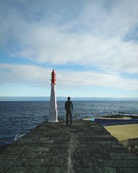 Rear view of man standing on lighthouse by sea against sky
