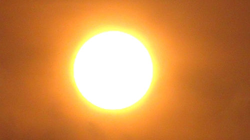 Low angle view of illuminated sun against orange sky