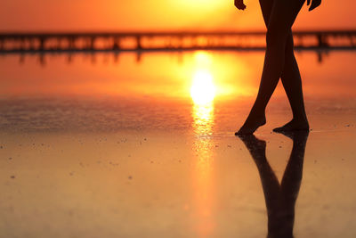 Low section of silhouette woman walking at beach during sunset