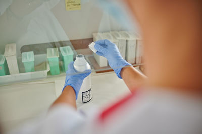 From above back view of crop unrecognizable medical specialist with plastic bottle of liquid near containers in lab