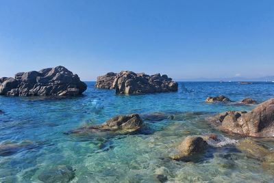 Scenic view of rocks in sea against clear blue sky