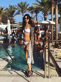 Full length portrait of young woman wearing bikini standing by swimming pool