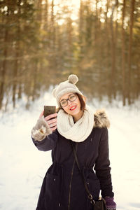 Young woman photographing taking selfie with mobile phone on snow covered field