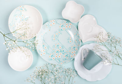 Spring layout of dishware white and with floral decor and white flowers on light blue. 