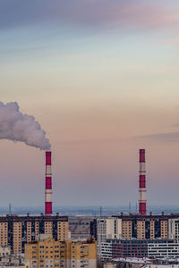 Smoke emitting from factory against sky at sunset