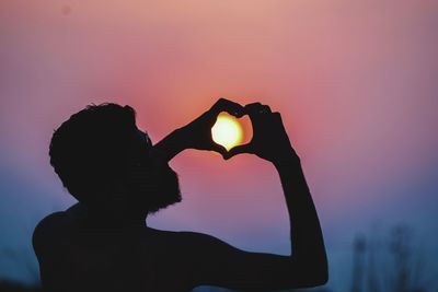 Rear view of man making heart shape against sun
