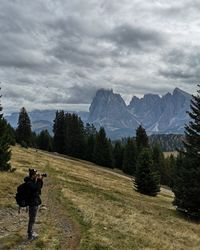 Side view of man photographing on mountain against cloudy sky