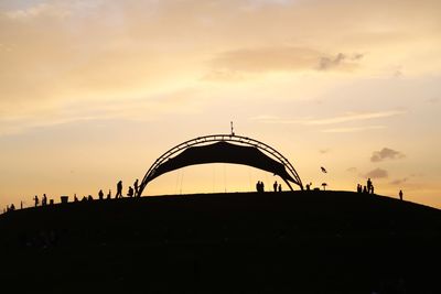 Silhouette of people on land against sky at sunset