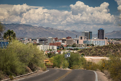 Road by buildings in city against sky