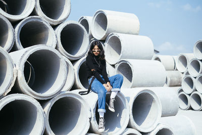 Portrait of boy standing by stack of pipes against sky