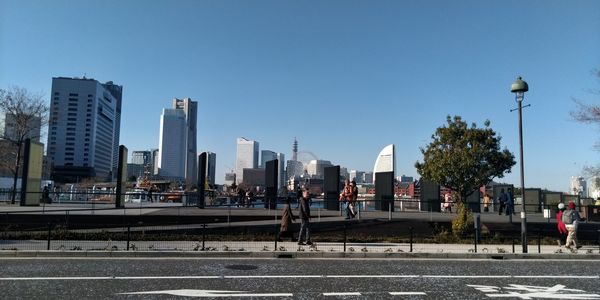 People on road by buildings against clear sky