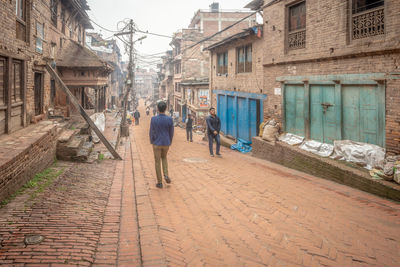 Rear view of man walking on footpath amidst buildings