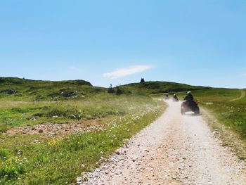 People riding motorcycle on road amidst field against sky