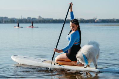 Woman with dreadlocks paddleboarding with dog snow-white japanese spitz on sup board on city lake