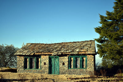 Old wooden house on field against clear blue sky
