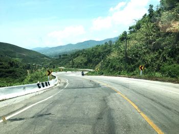 Empty road along trees and mountains against sky
