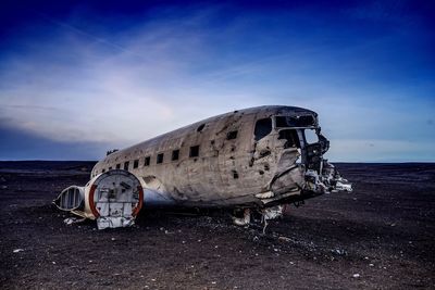 Abandoned airplane on sand at beach against sky