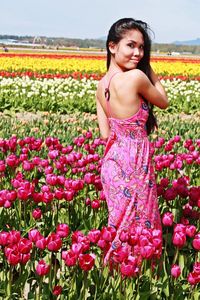 Portrait of young woman standing amidst tulips on sunny day