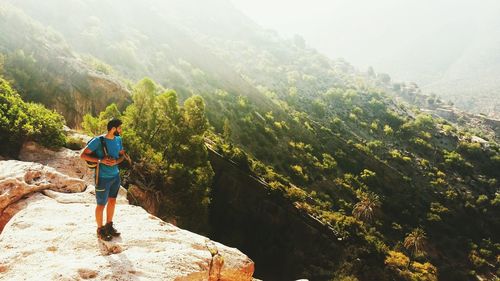 Full length of hiker on cliff looking at mountain