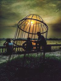 People sitting on grass against sky during sunset