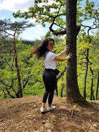 Full length of young woman standing on tree trunk