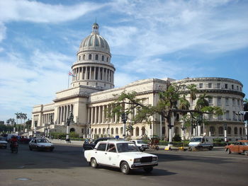 Cars on road by buildings against sky in city