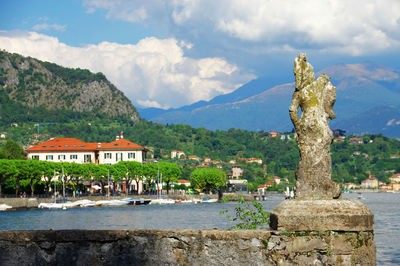 Old ruin statue on retaining wall at lake como against cloudy sky