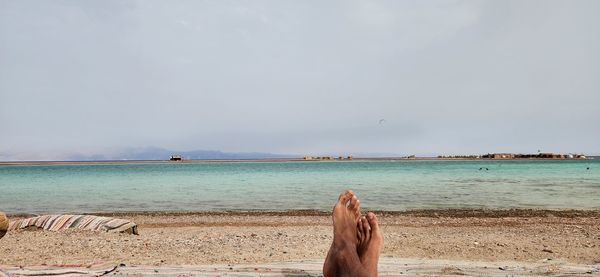 Low section of woman relaxing on beach against sky