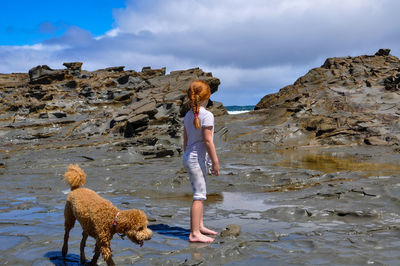 Full length of girl with dog on rock against sky