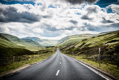 Road leading towards mountains against sky