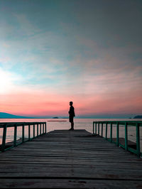 Silhouette man standing on pier by sea against sky during sunset