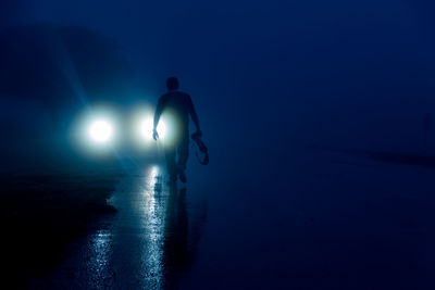 Silhouette people on illuminated street light against blue sky at night