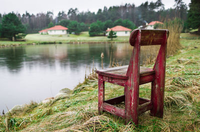 Abandoned chair on grass by water