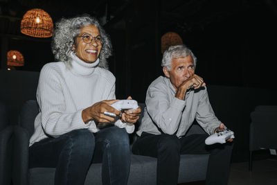 Smiling senior woman playing video game by male friend in gaming lounge
