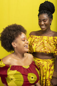 Portrait of two women against yellow background. they wear yellow and red colored clothes.