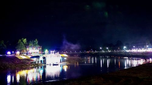 Illuminated buildings by river against sky at night