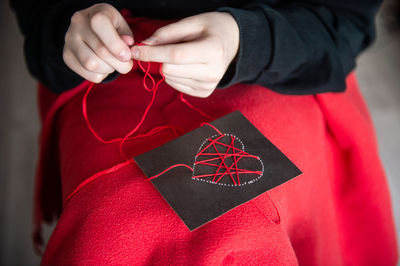 The child's hands make a card with a heart for mother's day with red threads